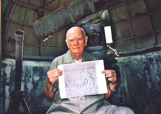 Sir Arthur Clarke, sitting next to the historic telescope, shows a photo of Crater Molesworth