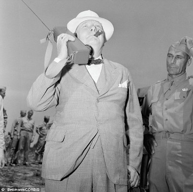 Churchill smokes a cigar as he holds a radio to his ear and watches the descent of American paratroopers during his visit at Fort Jackson, South Carolina.