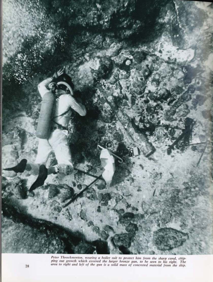 Peter Throckmorton, wearing a boiler suit to protect him from the sharp coral, chipping out growth which covered the larger bronze gun, to his right.